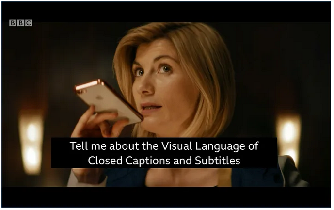 A dark, paused video image of a woman with blonde, shoulder-length hair looking up to the left while holding her apple cell phone and appearing to speak into the bottom of the phone with her mouth slightly open. Closed captioning on the photo says, "Tell me about the Visual Language of Closed Captions and Subtitles." 