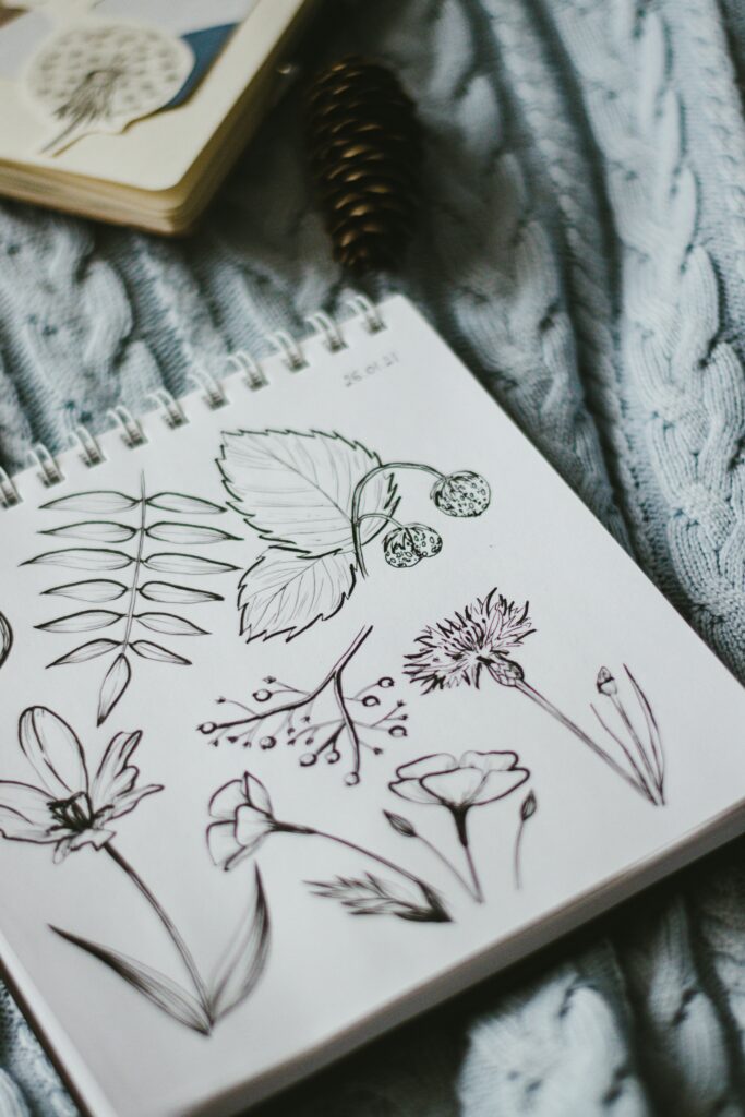 note pad with simple sketches in black ink of flowers, a tree branch, wild strawberries, and a leafy branch. Background is a cable-knit pale blue sweater.