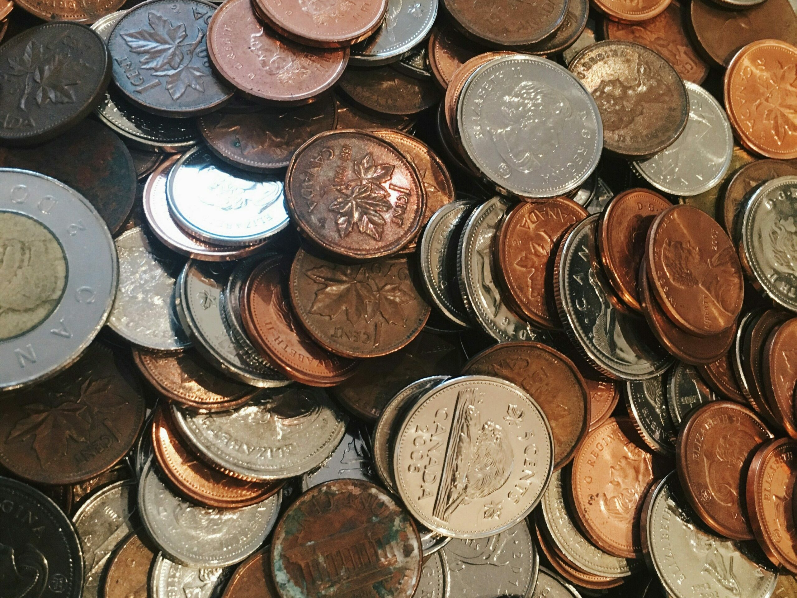 A pile of assorted Canadian coins, including pennies, nickels, dimes, and quarters. The coins feature various designs and different metals, creating a mix of copper, silver, and bronze hues.